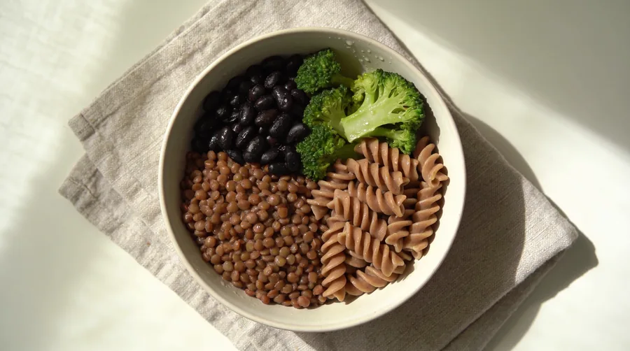 Overhead view of a lunch bowl with lentils, black beans, broccoli, and whole-wheat pasta as a high-fiber meal